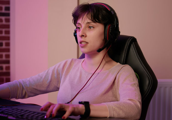 Young woman wearing a headset seated in a gaming chair, focused on her computer, representing ways women make men uncomfortable.