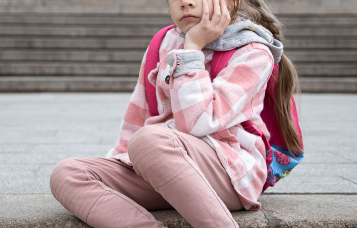 Young girl with backpack sitting on steps looking upset, illustrating parenting challenges and oversleeping nightmares.