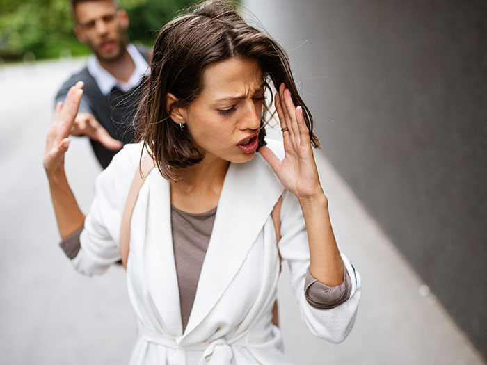 A woman looking disgusted, holding her hand to her ear, with a man reaching out behind her. This image depicts horrible first dates.