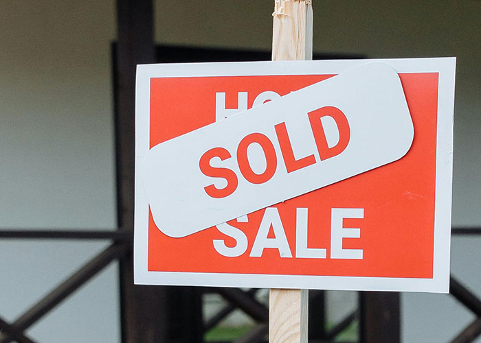 For sale sign with sold sticker on wooden post representing economy showing mixed signs of performance