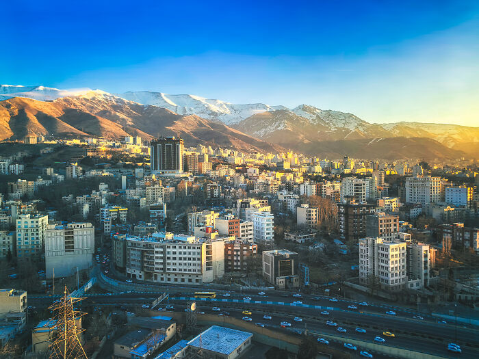 Aerial view of a bustling city with a highway, diverse buildings, and sunny snow mountains, highlighting worst work-life balance.