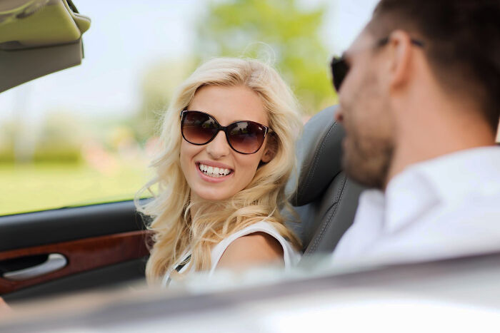 Blonde woman in sunglasses smiling in a convertible with a man. Discussing friendship betrayals and trust.