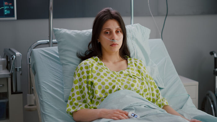 Young woman with nasal oxygen tube lying in hospital bed, illustrating random facts people learned about their bodies at the doctor.