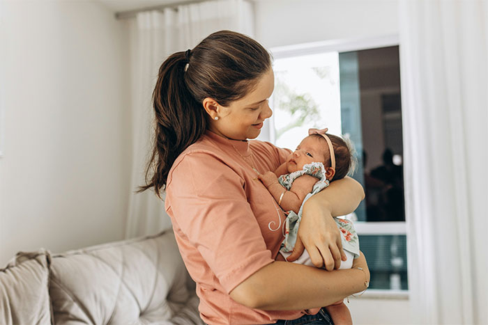Woman holding a baby in a cozy living room, sharing a crazy story about her mom like a soap opera.