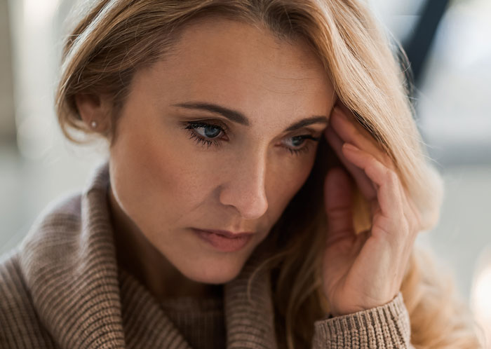 Worried woman reflecting on a teacher grabbing kids in front of mom, showing concern and disbelief in a close-up portrait.