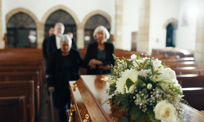 Floral arrangement on casket with mourners walking solemnly in a church, reflecting feelings of parenting nightmares and regret.