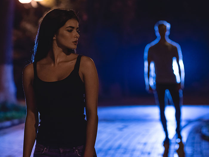 A woman glances warily at a blurred, glowing figure in the distance, portraying a horrible first date scenario.