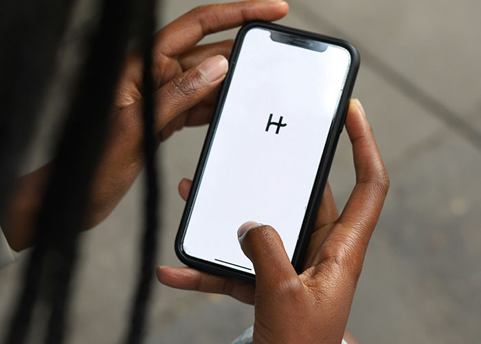 Person holding smartphone displaying a minimal black and white app logo, highlighting signs of the economy not doing well.