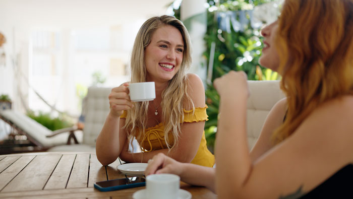 Two women enjoying coffee outdoors. One smiles, holding a cup. Could be a moment when dating revealed someone's true dumbness.