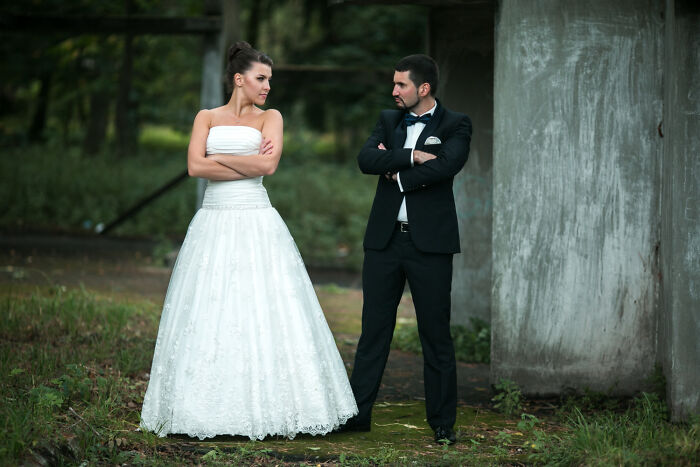 Bride and groom standing outdoors with arms crossed, showing tension that hints at a future breakup at the wedding.