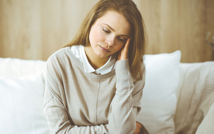 Worried mom sitting indoors, reflecting on her husband being awesome to her but a jerk to their kids.