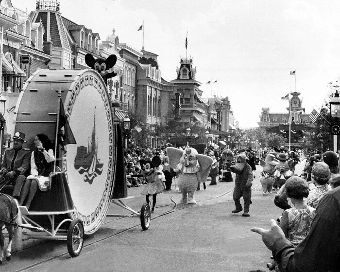 Black and white photo of a vintage Disney parade featuring classic characters and crowds on Main Street USA.