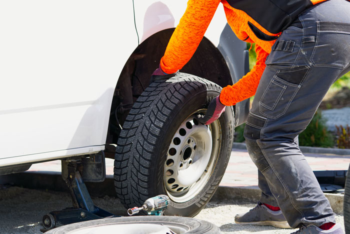Person wearing bright orange gloves and dark pants changing a car tire, illustrating unhinged and wild ways women make men feel uncomfortable.