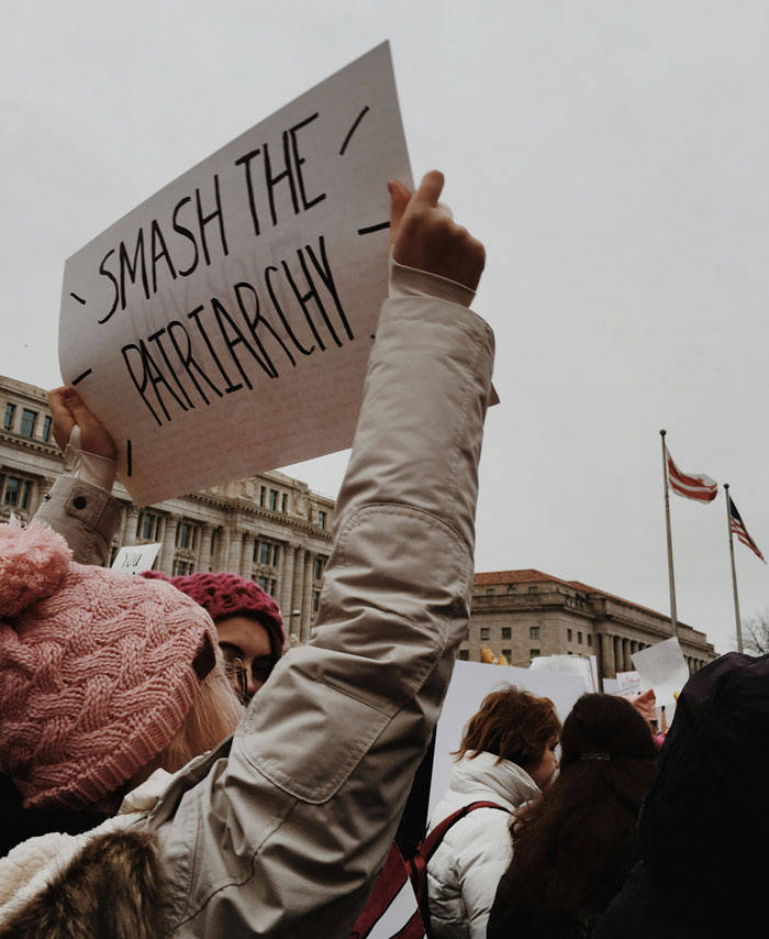 Woman holding a sign that says smash the patriarchy during a protest about things women are tired of explaining to men.