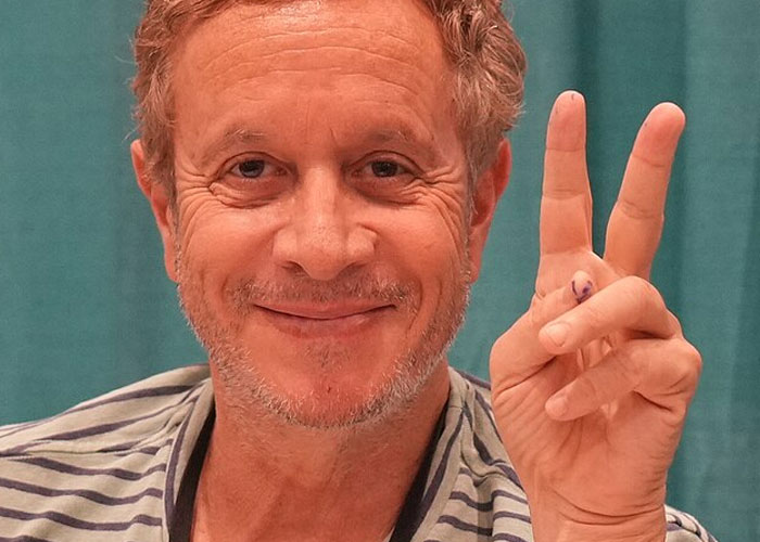 Smiling man with curly hair making peace sign, illustrating beloved celebrities who are not that nice in real life.