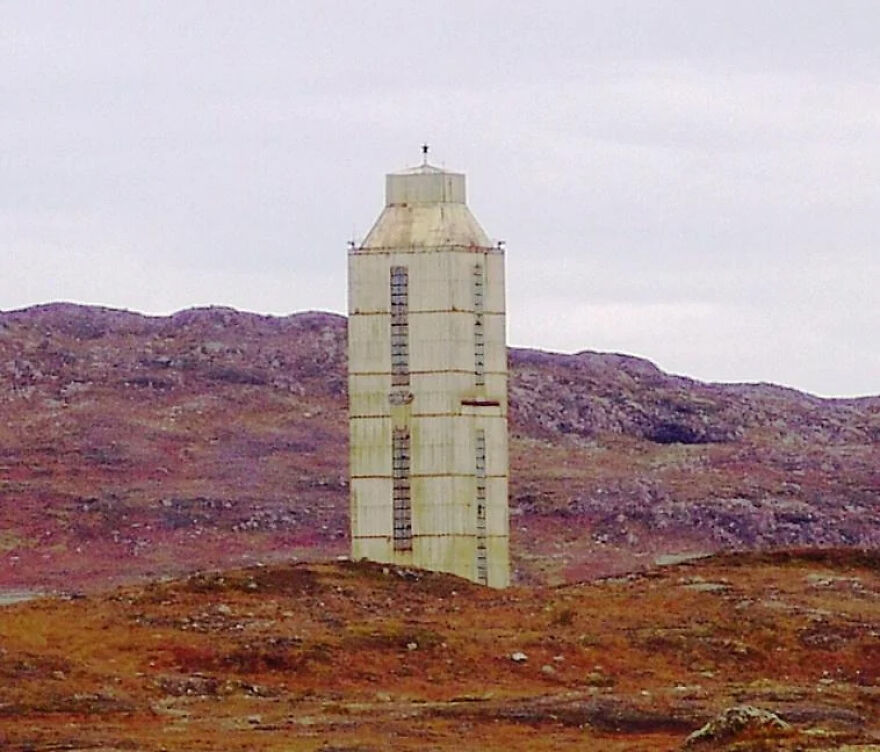 A stark, tall white tower stands in a rugged, reddish-brown landscape under an overcast sky, showcasing tough security.