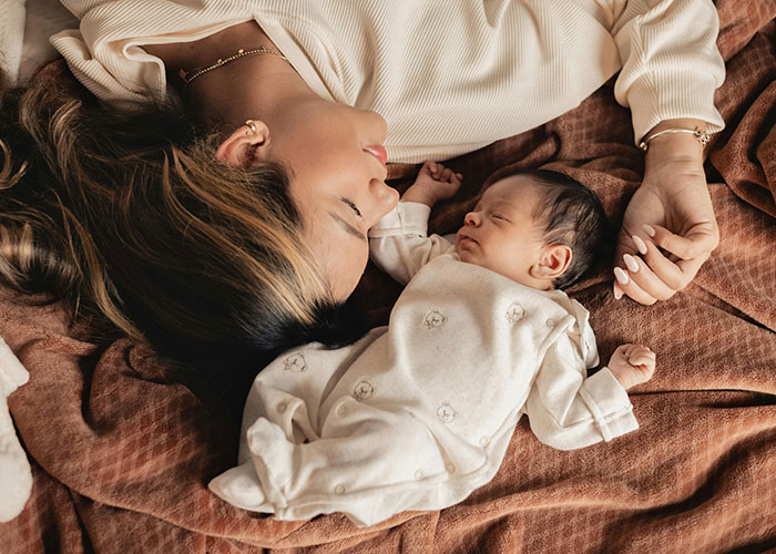 Mother and sleeping baby lying on bed, illustrating things that are a lot more dangerous than they seem in everyday life.