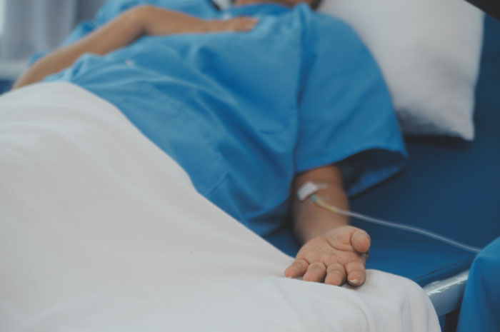 Person lying in hospital bed with IV drip, symbolizing consequences of petty karma served to their boss.