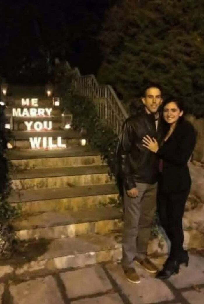 A weird image of a couple posing by steps illuminated with 'ME MARRY YOU WILL' creating a hmmm moment.