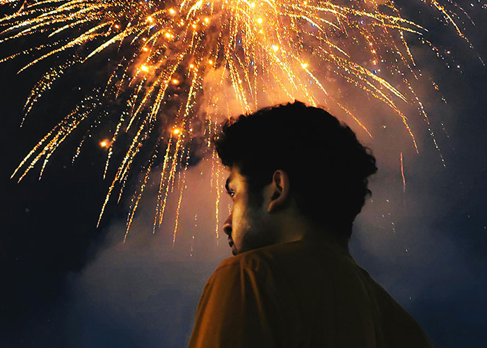 Young man looking at bright fireworks at night, illustrating random signs that show the economy is not doing well.