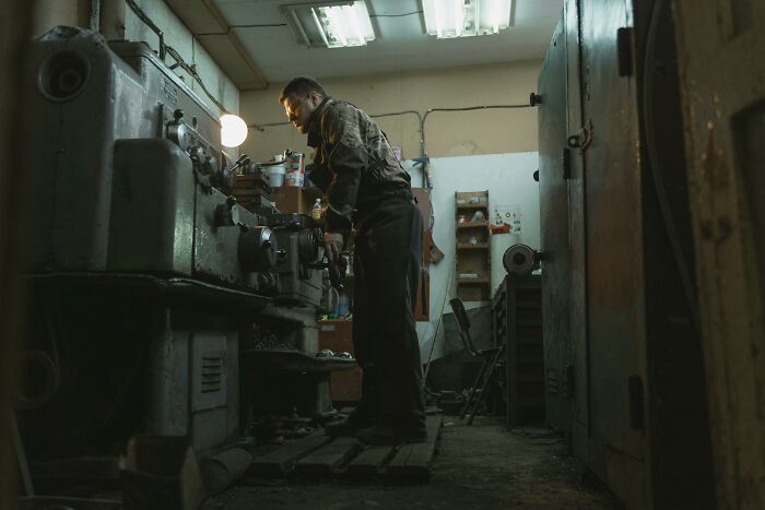 A worker operates heavy machinery in a dimly lit workshop, highlighting a potential workplace incident scene.