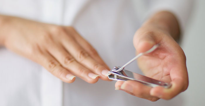 A person's hands, one using a nail clipper on a fingernail. This illustrates a gross office story about bad coworker habits.