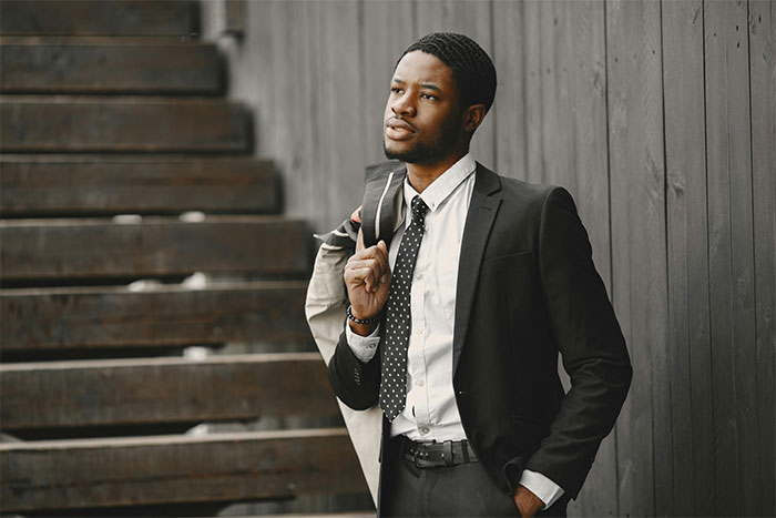 Young man in a suit looking thoughtful outside near stairs, illustrating an ex-girlfriend cheating on guy scenario.