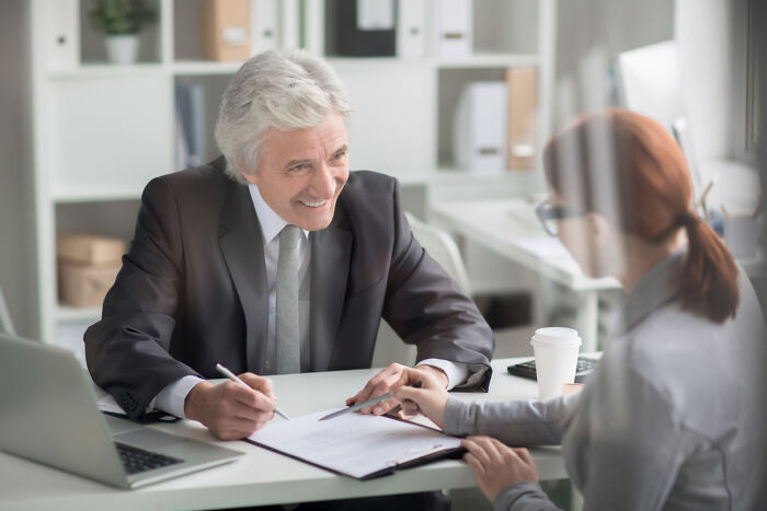 Senior businessman and young woman discussing projects at office desk, highlighting jobs AI can’t touch.