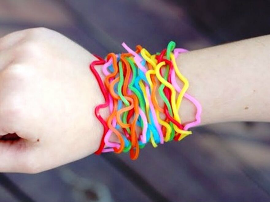 A person's wrist adorned with numerous colorful rubber band bracelets, reminiscent of childhood fun and taking a trip down memory lane.