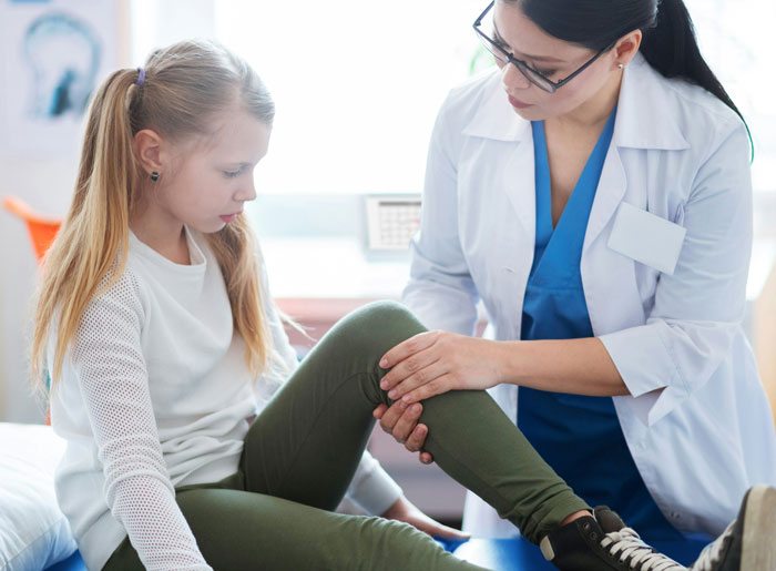 Teacher examining young girl's leg in a clinical setting, illustrating teacher grabs kids incident discussed online.