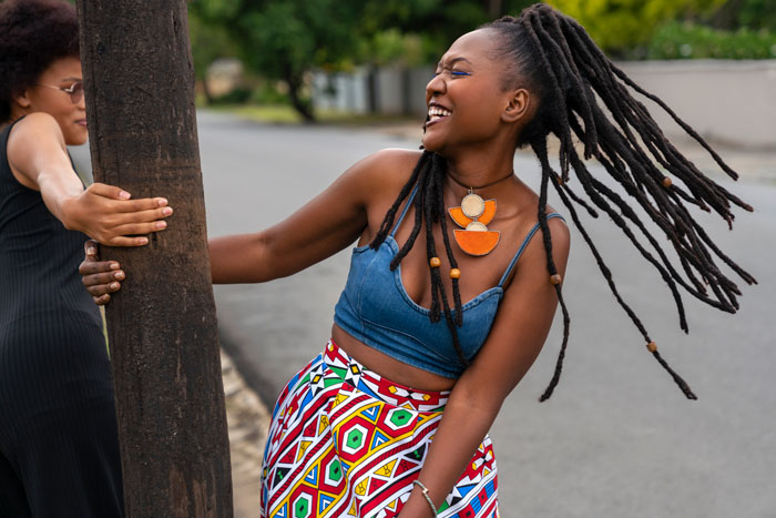 Two Black women, one in a denim top and colorful skirt, laughing. Showcasing favorite things about Black people.
