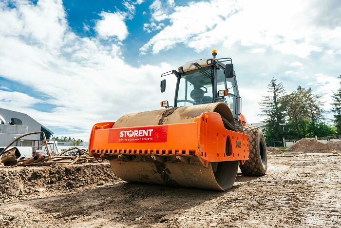 An orange road roller on a construction site under a partly cloudy sky, relevant to workplace incidents.