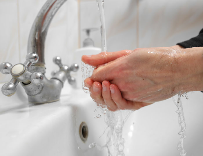 Hands washing under running water in a white sink, emphasizing hygiene in shared workspace environments. Gross office stories.