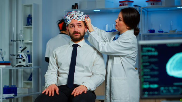 A scientist adjusts an EEG cap on a man in a white shirt and tie. Wildest rumours involve brain activity.