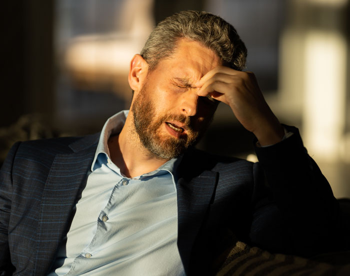 Man in a suit holding his forehead and looking uncomfortable, illustrating how women make men feel uneasy.