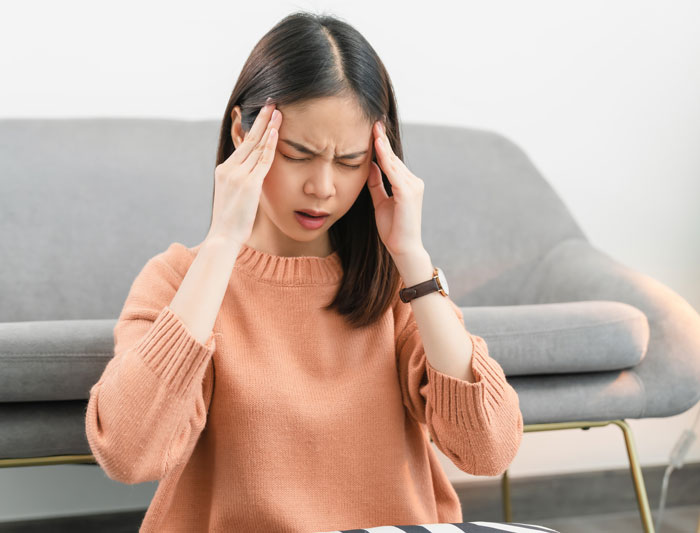 Woman in a peach sweater holding her temples, expressing frustration, related to things women are tired of explaining to men.