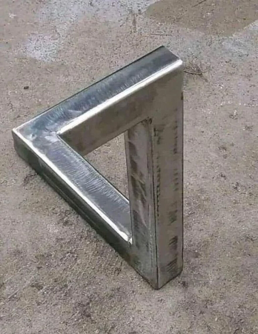 Metallic Penrose triangle on concrete, a classic optical illusion. Brain-bending visual trick.