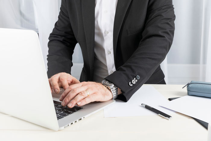 Man in black suit typing on laptop at desk, representing petty karma served to bosses in workplace situations.