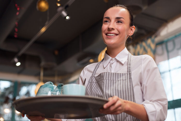 Smiling woman waitress holding a tray inside a café, capturing one of the wild ways women make men feel very uncomfortable.