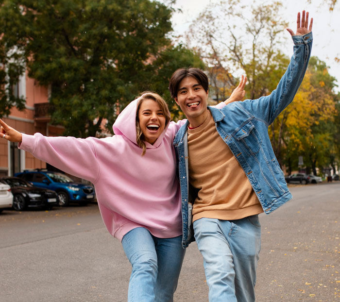Young woman and man outdoors laughing and posing together, expressing things women are tired of explaining to men.