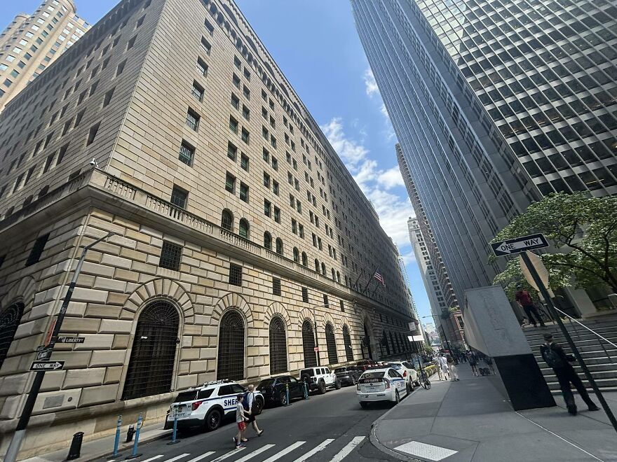 The World's Toughest Security protecting a large, stone building on a city street with modern skyscrapers and police vehicles.
