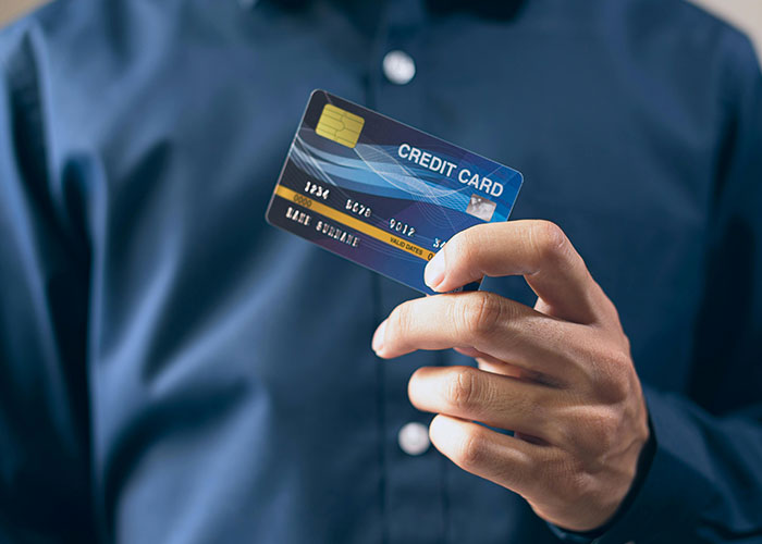 Person in dark shirt holding a credit card, illustrating signs that the economy is not doing well.