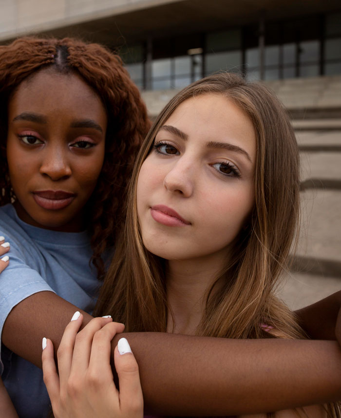 Two young women, one Black and one white, embracing. The white woman has her arm around the Black woman.