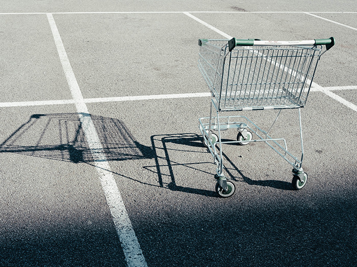 Empty shopping cart in an outdoor parking lot casting a shadow, symbolizing rude customers learning the hard way.