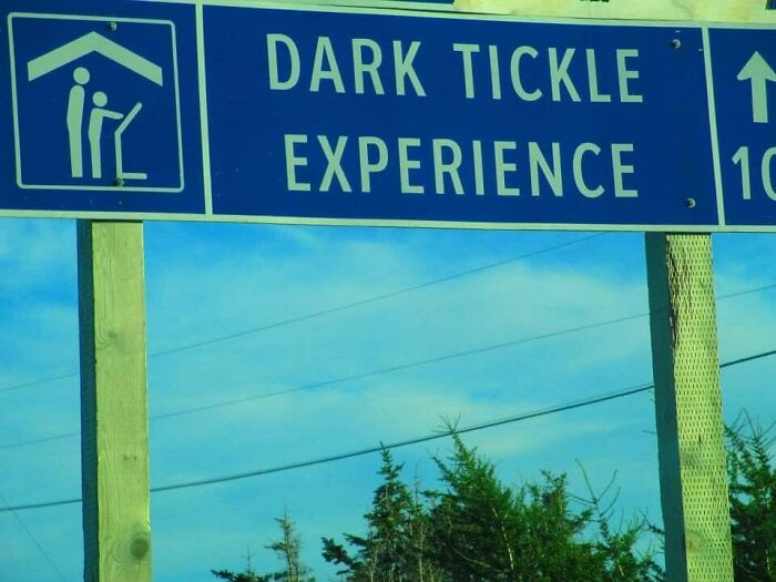 Road sign reading dark tickle experience with a confusing symbol of two figures under a roof in a weird image.
