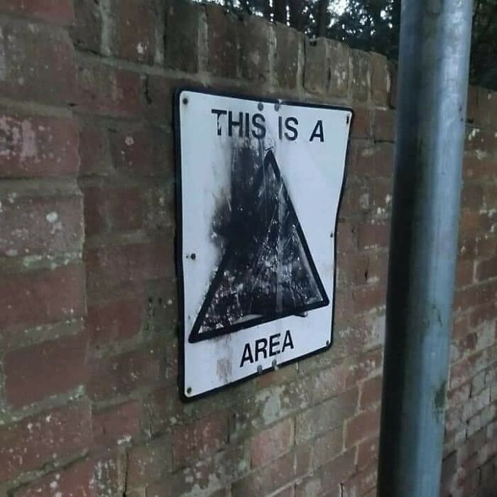 Faded and damaged warning sign on brick wall in a confusing and unhinged image that gets weirder with time.