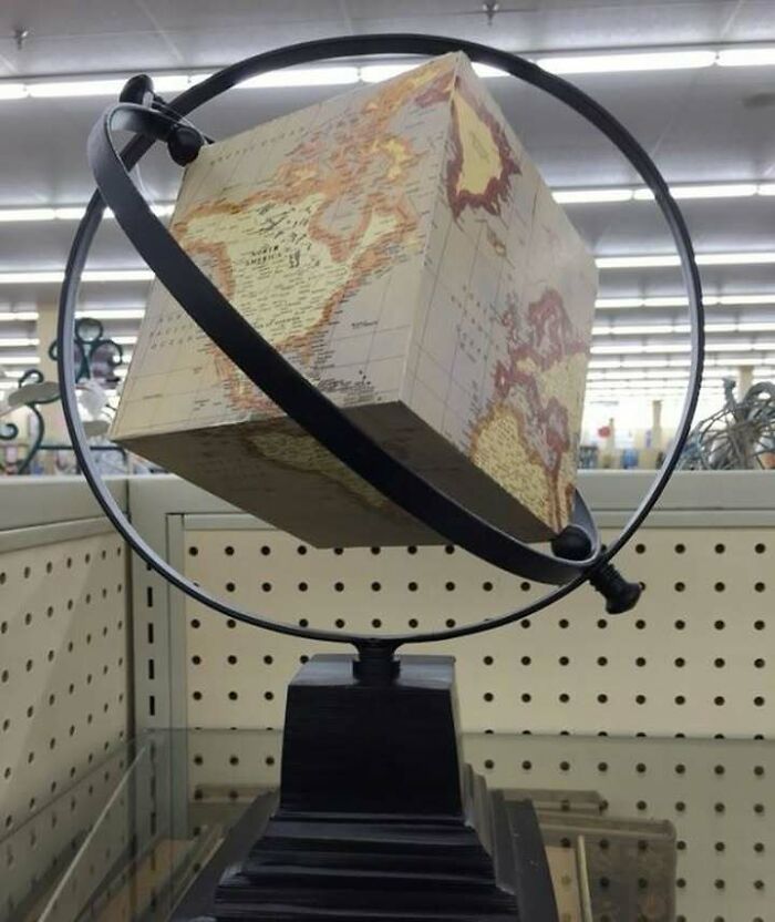 Cube-shaped globe with map design inside a metal ring stand, showcasing a confusing and unhinged object in a store display.