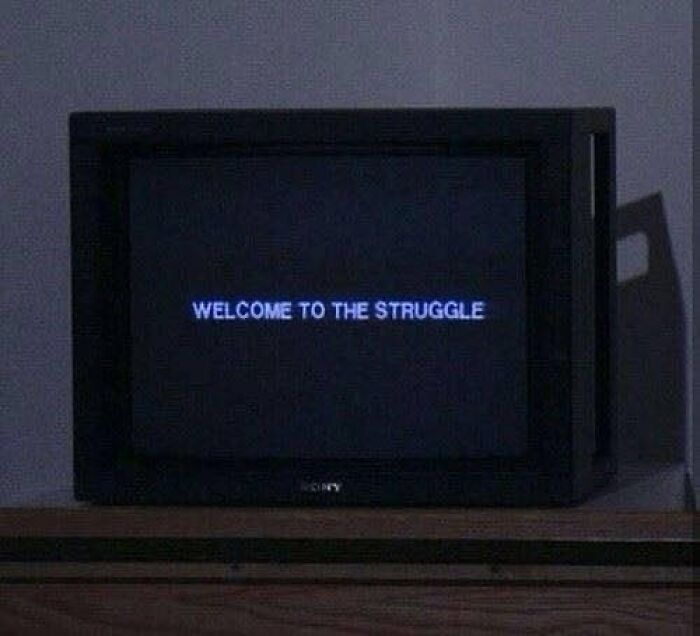 Old Sony TV displaying blue text saying welcome to the struggle in a dimly lit room, confusing and unhinged image.