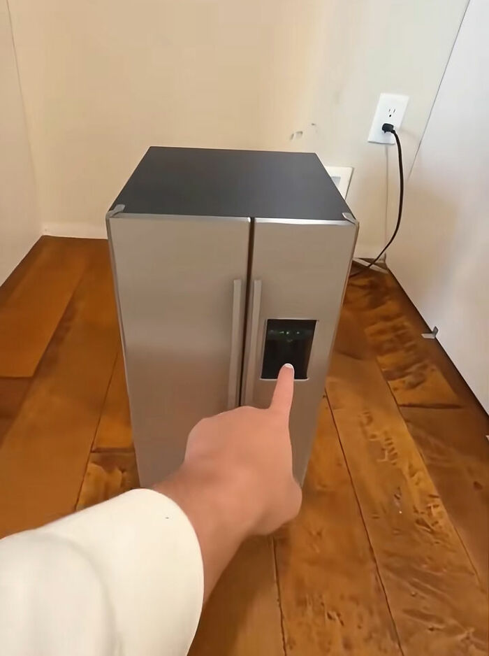 Person pointing at a miniature silver fridge on wooden floor illustrating a funny Temu order experience.