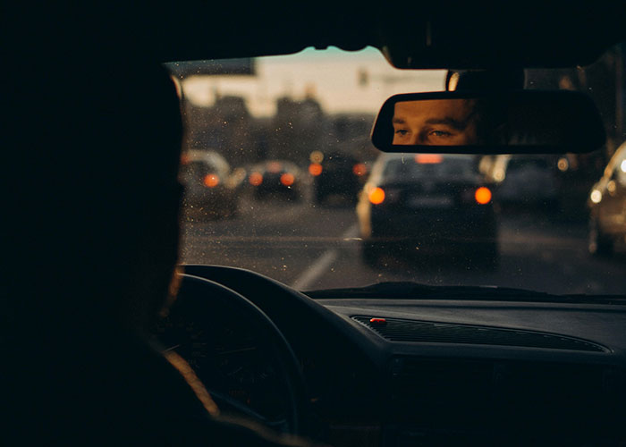 Driver seen through rearview mirror in busy traffic, illustrating dangers that are a lot more serious than they seem